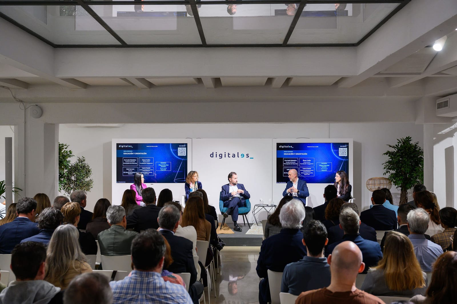 Público asistiendo a una mesa redonda con ponentes en el escenario de V22